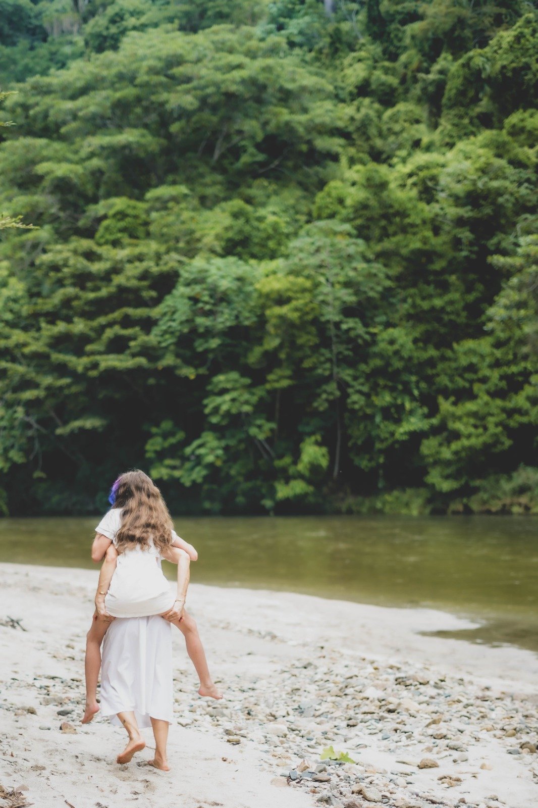 Madre cargando a su hija caminando hacia un río